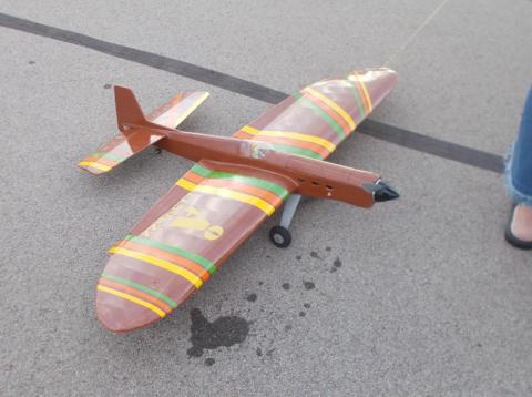 Model airplane with brown, yellow, and green stripes on a pavement.