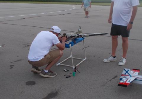 Two men adjusting a model airplane on an airfield.