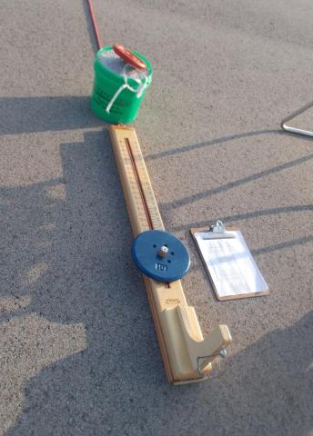 A balance beam with weight and clipboard on asphalt.