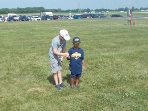 Two boys in a grassy field, one helping the other.