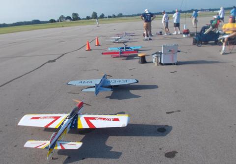 Model airplanes lined up on a runway with people in the background.