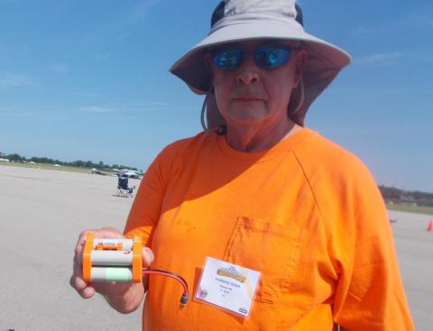 Man in orange shirt holds an electronic device at an outdoor event.