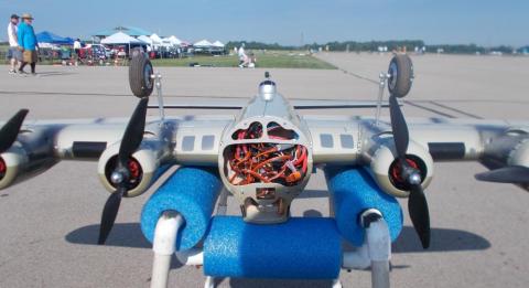 Model airplane with visible wiring, resting on foam supports on a runway.
