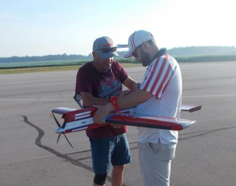 Two men prepare a red model airplane on an airstrip.