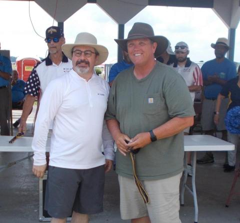 Two men wearing hats smiling, standing under a pavilion.
