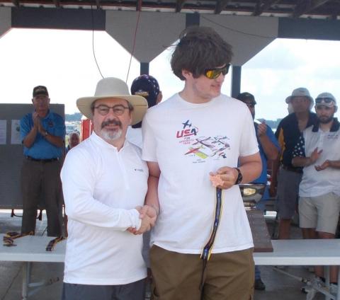 Two men shaking hands at an outdoor event, one wearing a hat.