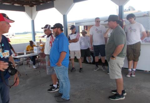 Group of people standing under a canopy, casually talking.