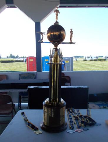 A large gold trophy with a globe and figures on top, on a table outside.