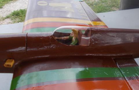 Model airplane with brown body, colorful stripes, and small pilot figure in the cockpit.