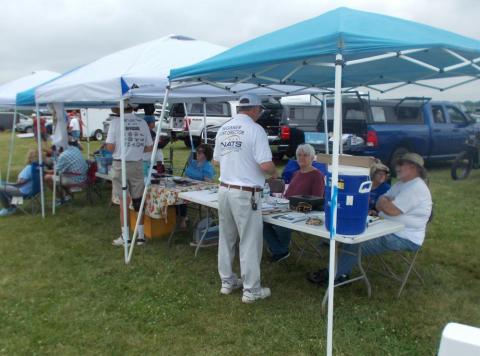 Outdoor gathering under canopies, people seated, talking, and sharing food.