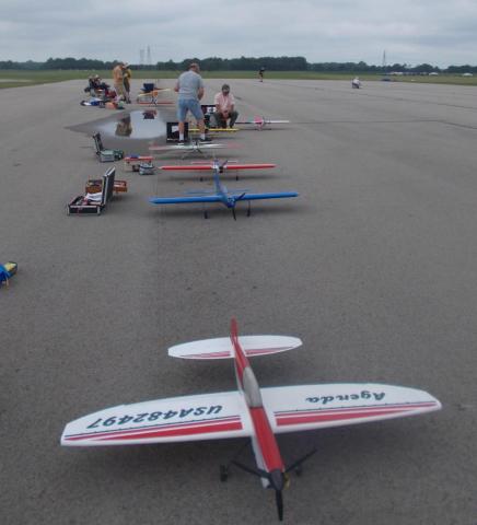 Model airplanes lined up on an airport runway, people gathered in the distance.
