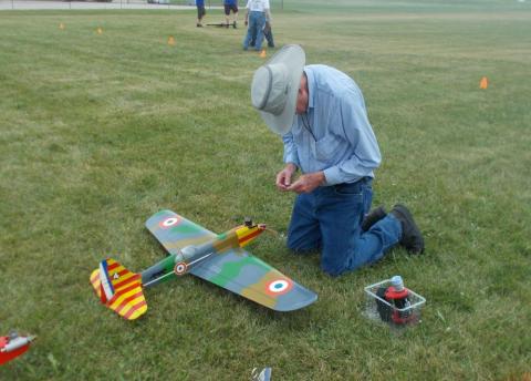 Man kneeling on grass, adjusting remote-controlled model airplane.