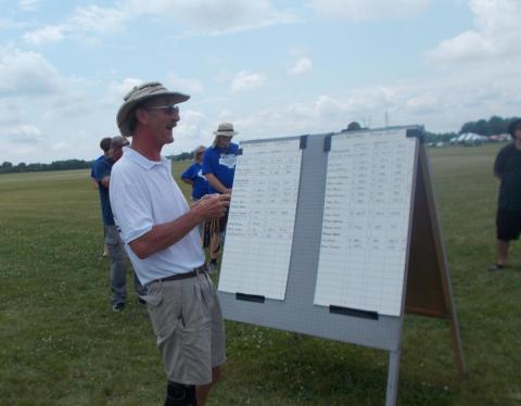 Man in hat stands near a scoreboard outdoors, cloudy sky.
