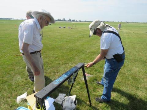 Two men setting up a model rocket on a grassy field.