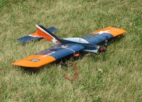 Remote control airplane with orange and blue wings on grass.