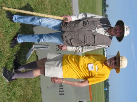 Two people wearing sun hats and casual outdoor attire, smiling on a grassy field.