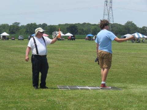 Two men in a field, each holding a toy rocket launcher, facing away from each other.