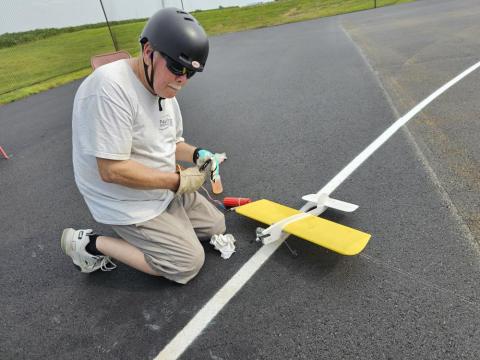 Man kneeling beside a small yellow model plane on a runway.