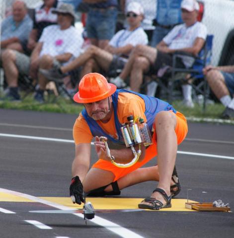 Man in orange gear painting lines on a sports field, seated crowd in background.