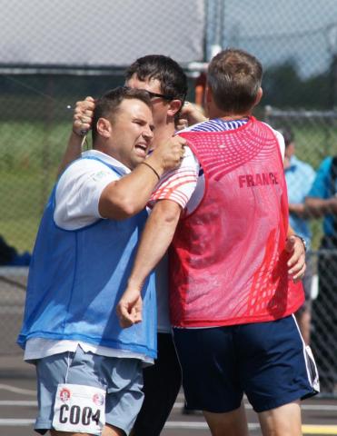 Three men in sports attire hugging emotionally on a sports field.