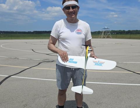 Man holding model airplane on a sunny day at an outdoor airfield.
