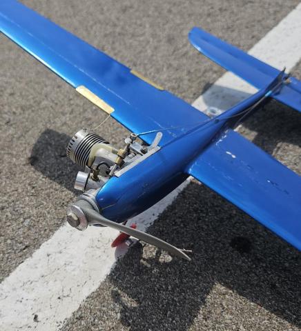 Blue model airplane on asphalt, with a visible engine and propeller.