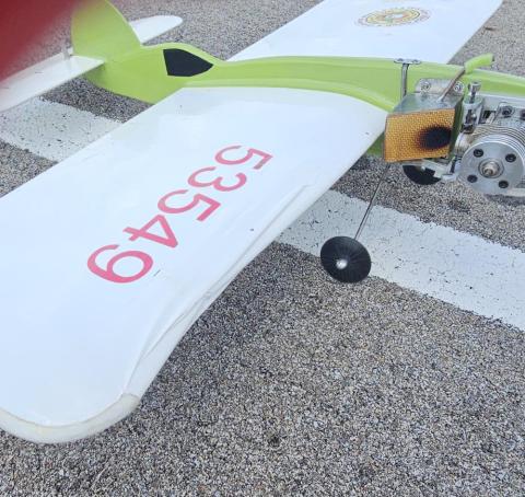 Small model airplane with green and white wings, resting on a gravel surface.