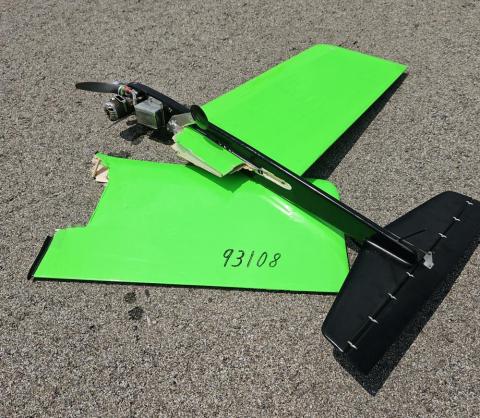 Bright green and black broken drone rests on asphalt.