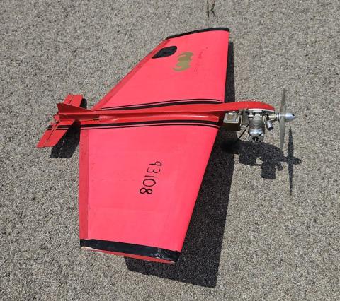 Red and black model airplane with visible propeller, on a textured surface.