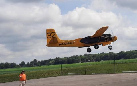 A small yellow aircraft with the number 32 takes off near a grassy field.
