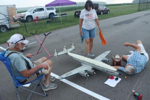 Model airplanes on the ground with people inspecting them in an outdoor setting.