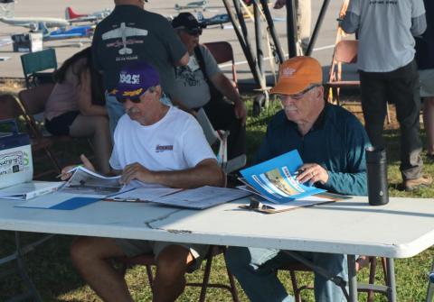 Two men sitting at an outdoor table, reviewing documents.