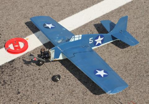 Model blue airplane with white stars on pavement, near red disc.