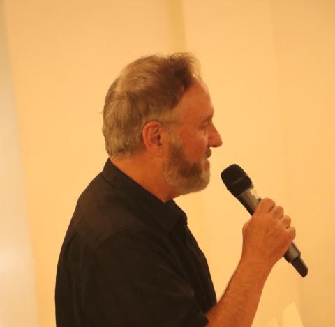 Man speaking into a microphone against a light-colored background.