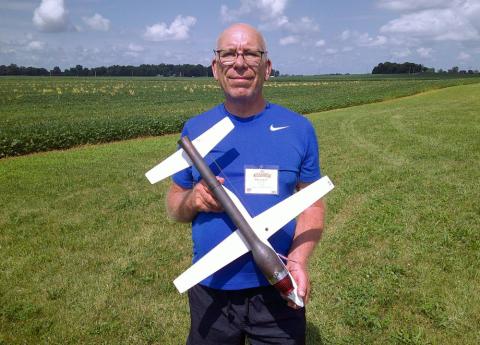 Man holding a model airplane on a grassy field under a partly cloudy sky.
