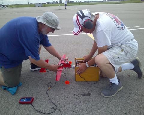 Two men on a runway setting up a red model airplane.