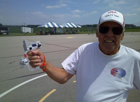 Elderly man outdoors, smiling, holding a small model airplane controller.
