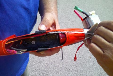 Hands holding a red remote-controlled plane with exposed battery and wiring.