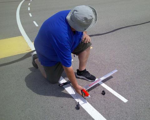 Man kneels on asphalt, measuring parking lines with a ruler.