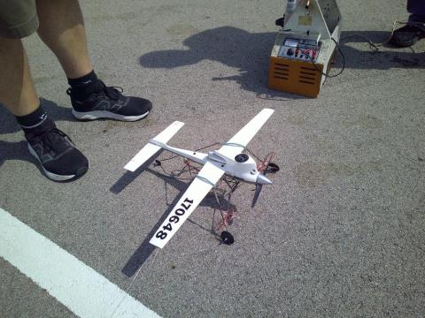 White model airplane on pavement, two people standing nearby.