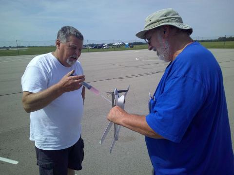 Two men standing on an airstrip examining a small rocket.