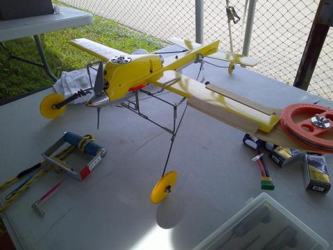 Model airplane with yellow wings on a table near a fence.