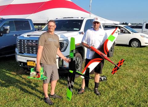 Two men holding colorful model airplanes in front of a parked truck.