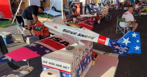 Model airplanes displayed on tables at an outdoor event with people nearby.