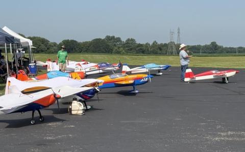 Model airplanes on a tarmac, people nearby on a sunny day.