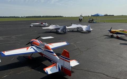 Remote-controlled planes on an airfield under a clear sky.