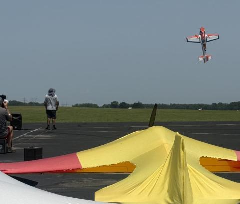 Man controls flying model aircraft at an airfield.