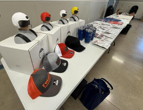 Caps and helmet replicas displayed on a table with promotional items.