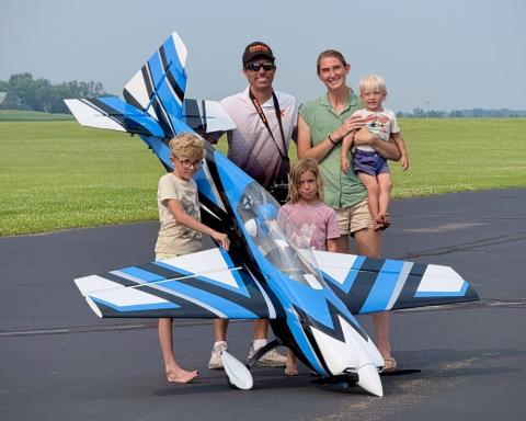 Family with children and a large blue model airplane outdoors.