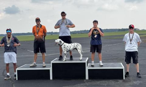 Five people and a Dalmatian stand on a podium with medals.
